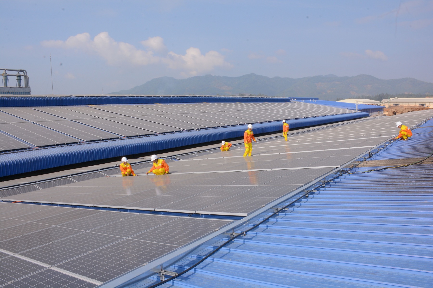 Technicians in protective equipment servicing a large rooftop solar array at an industrial site